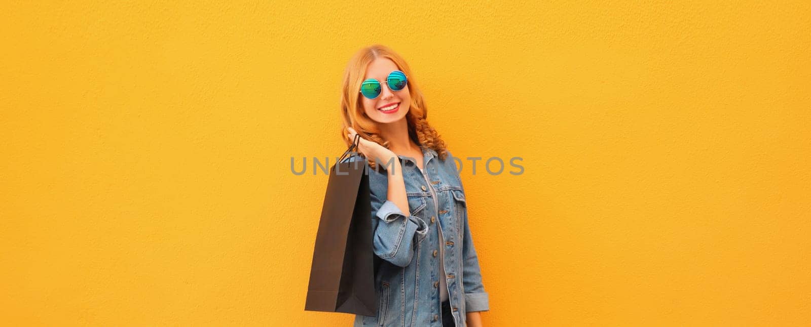 Stylish beautiful happy smiling young woman posing with black shopping bags on yellow studio background