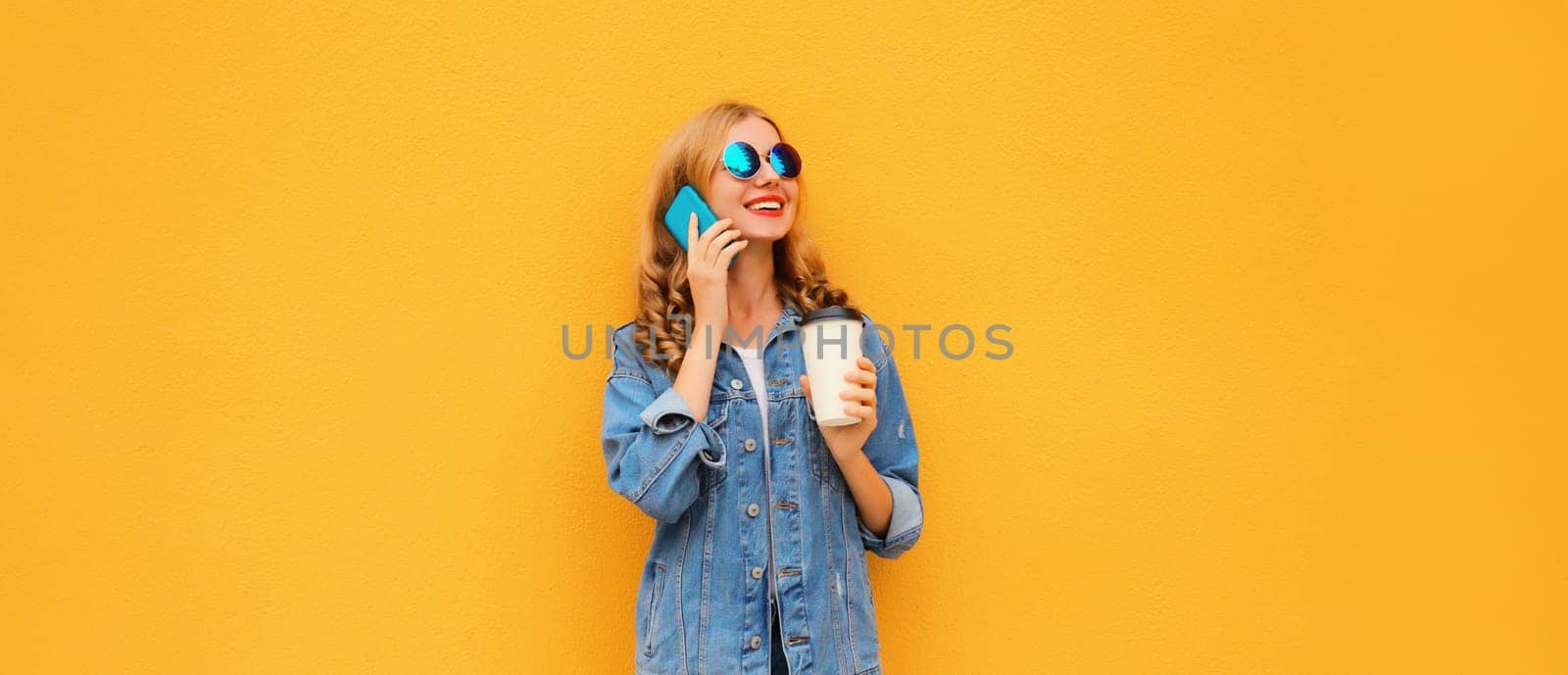 Modern happy young woman calling on mobile phone in denim jacket on yellow studio background