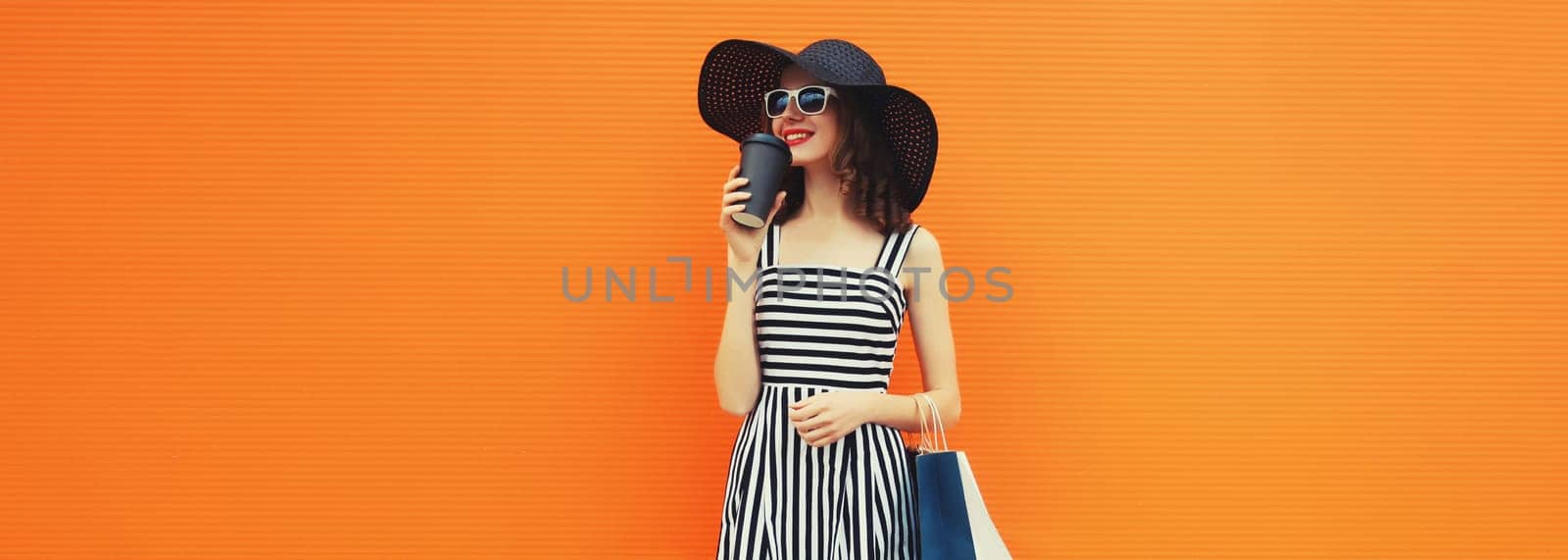 Beautiful happy woman model with shopping bags in summer black hat, dress on orange background by Rohappy