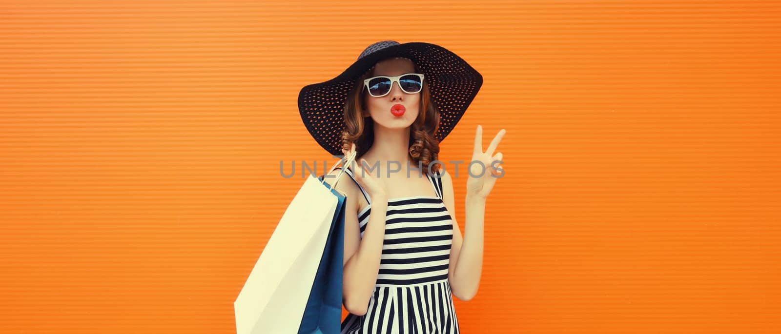 Beautiful happy woman model with shopping bags in summer black hat, dress on orange background by Rohappy