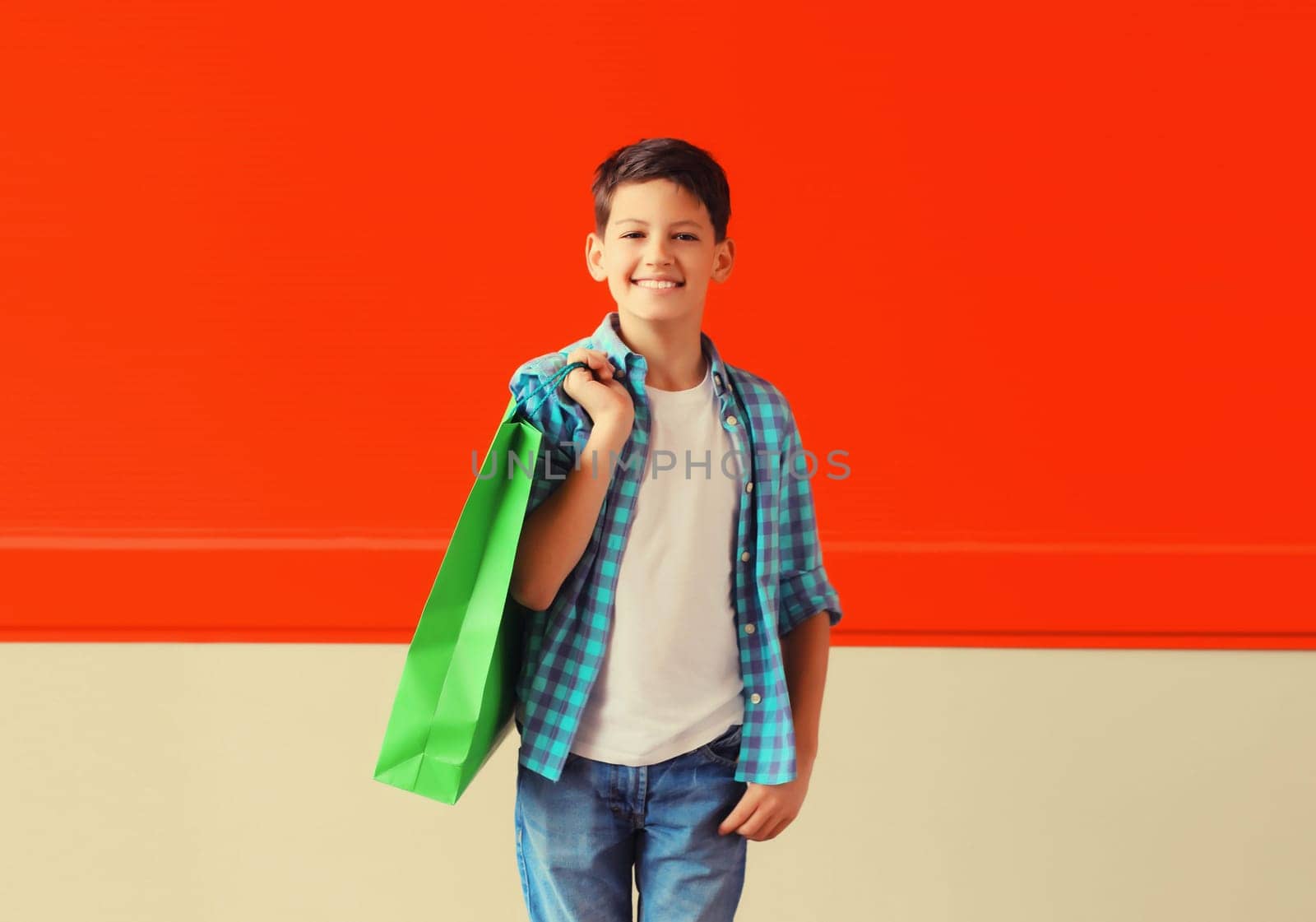 Portrait of happy smiling boy teenager with shopping bag in the city on red background
