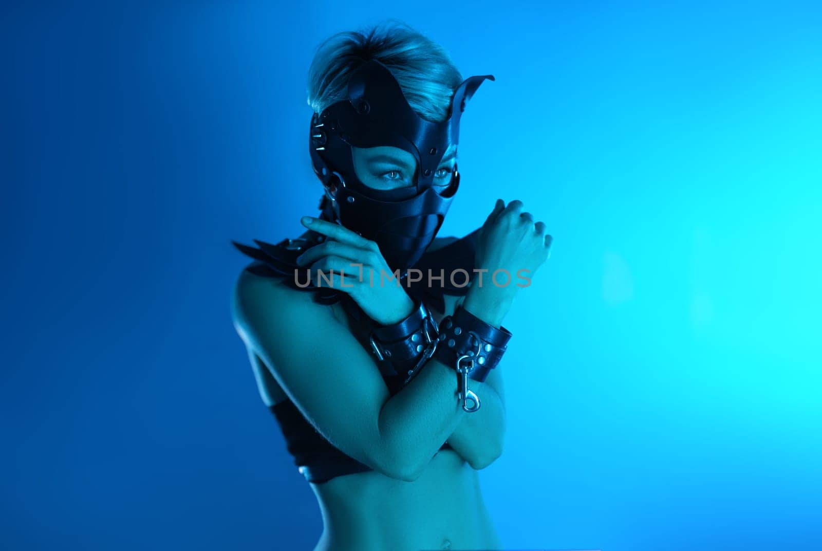 portrait of a hot sexy girl in a leather cat mask and muzzled in bdsm handcuffs on neon blue light by Rotozey