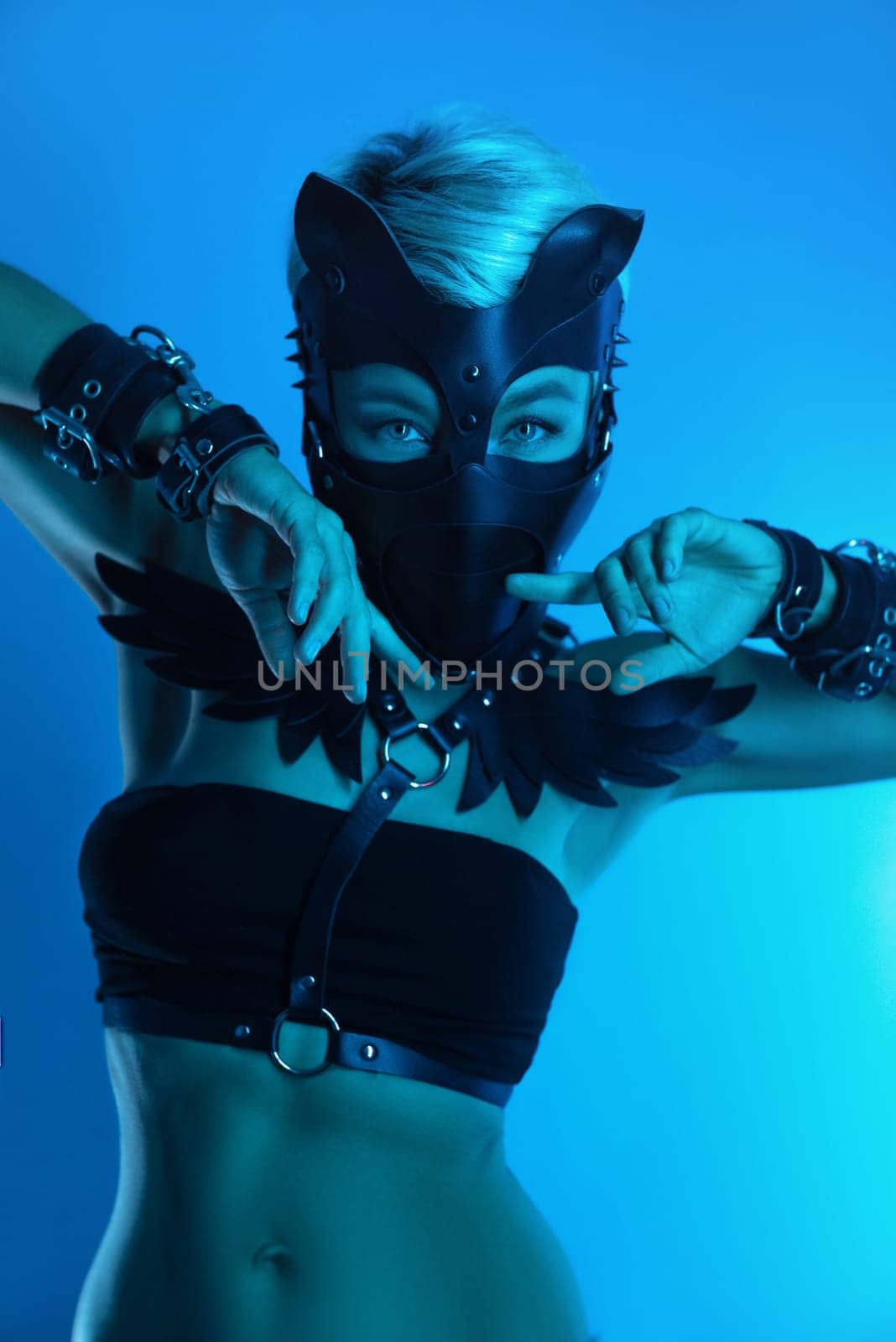 portrait of a hot sexy girl in a leather cat mask and muzzled in bdsm handcuffs on neon blue light by Rotozey