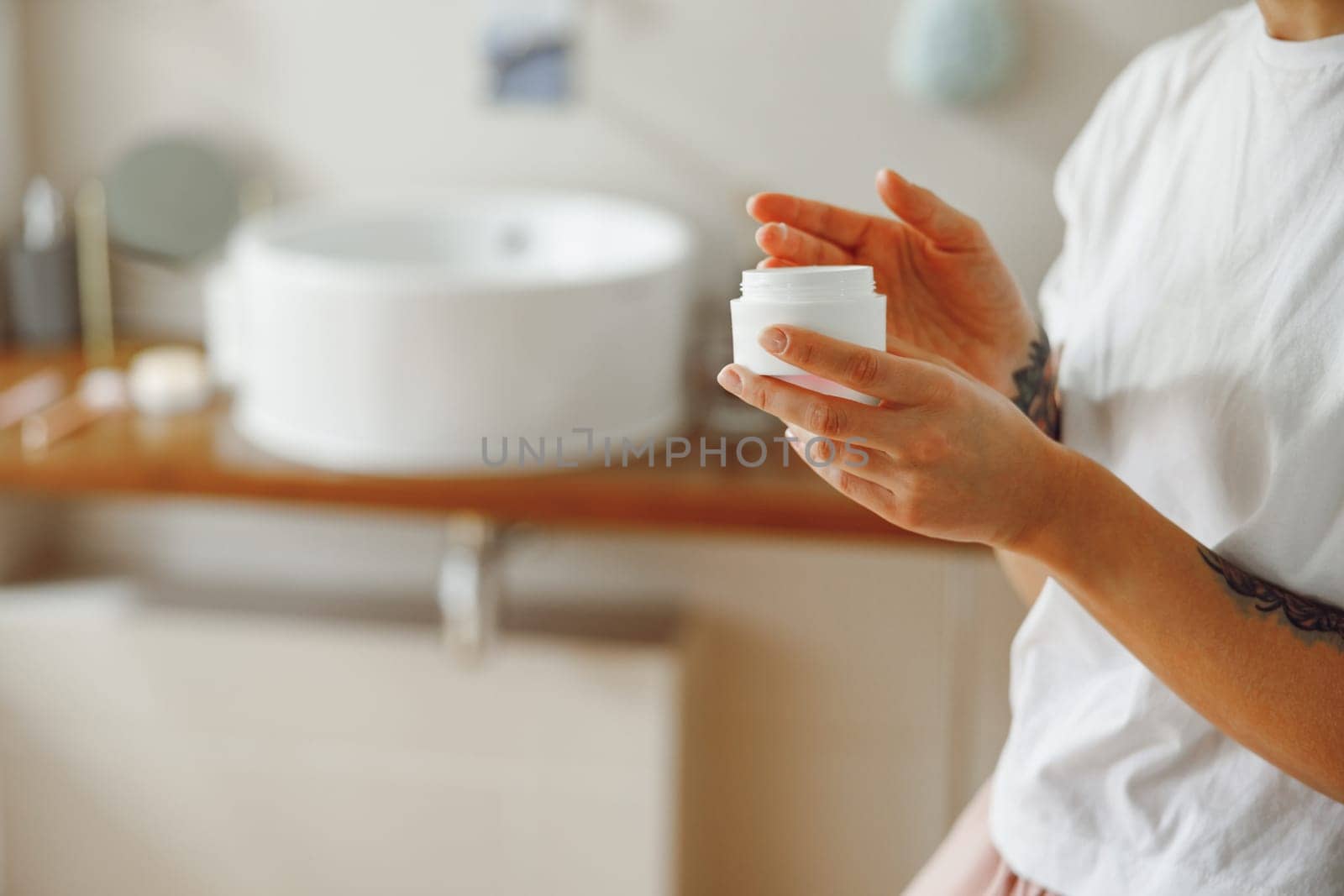 Close up of woman opening jar with face cream while standing in bathroom. High quality photo