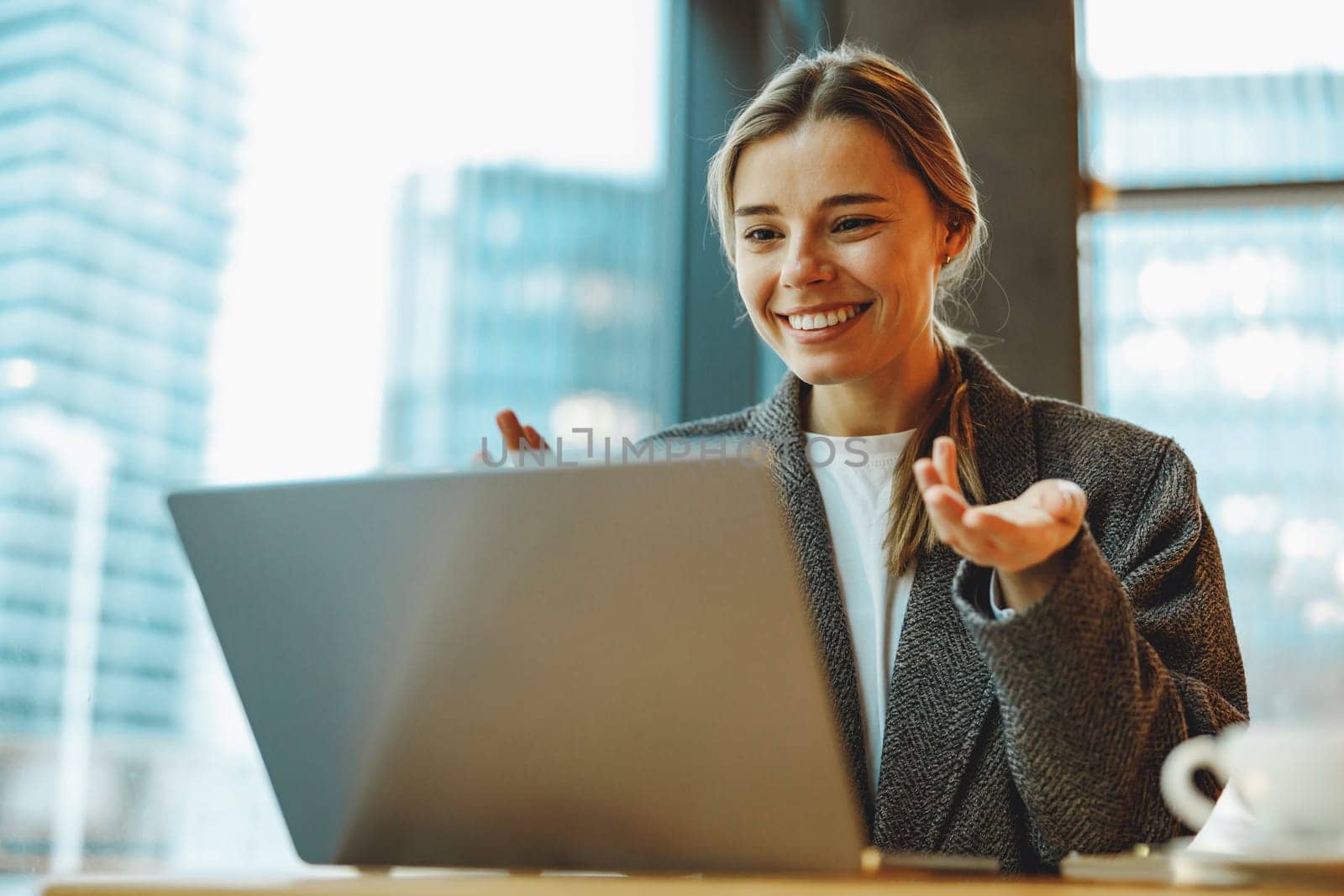 Young female manager talking via video call with client while use laptop sitting in cafe