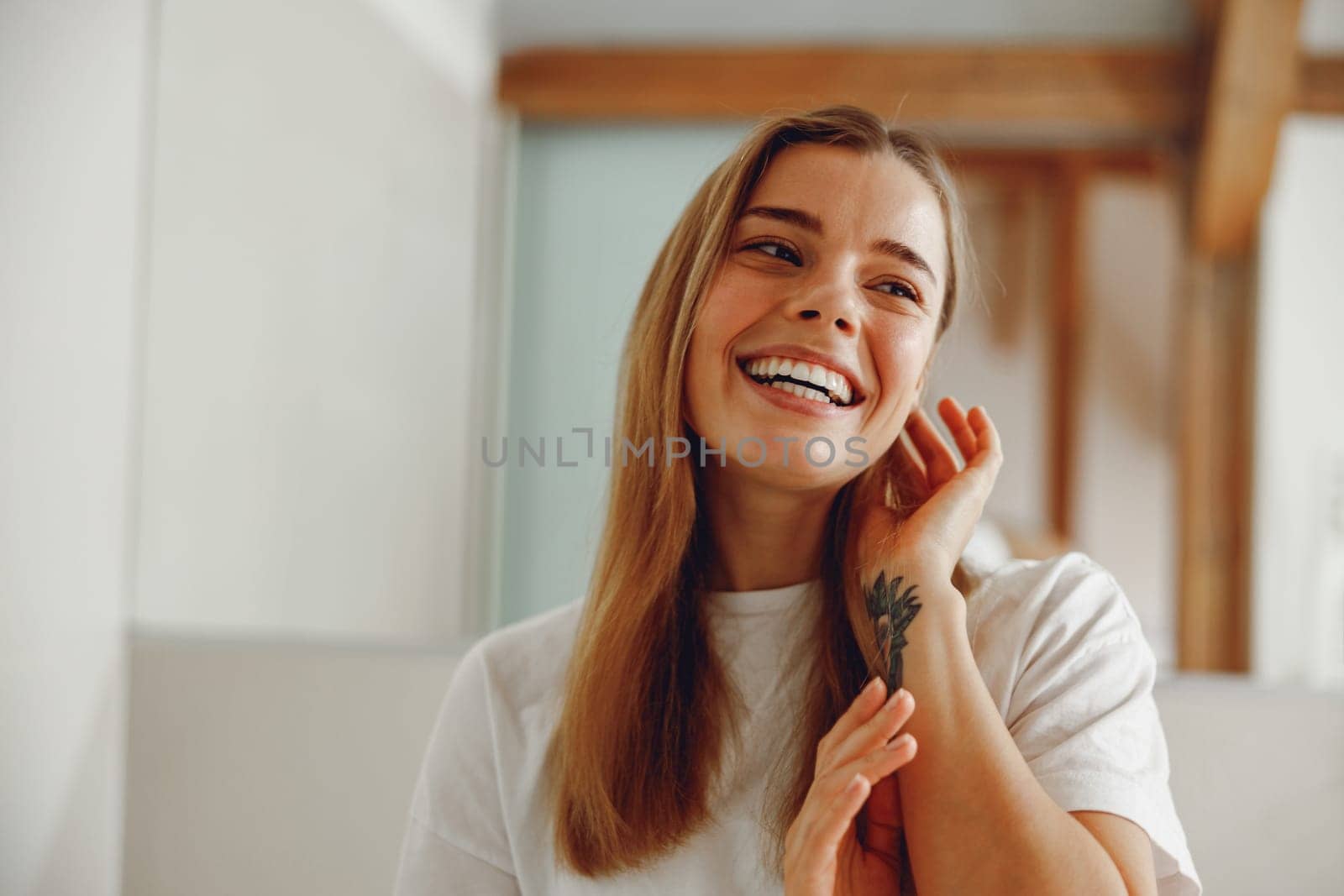 Smiling young woman touching face while standing in bathroom and looks away by Yaroslav_astakhov