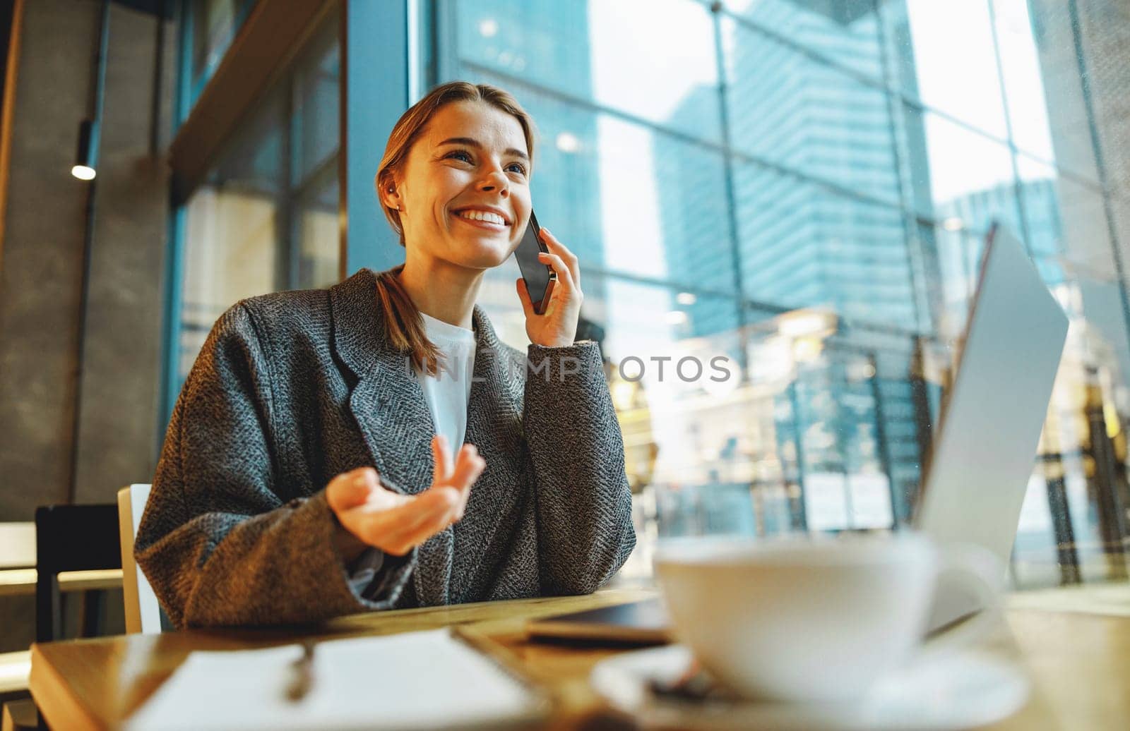 Young female freelancer talking with client and work on laptop in cafe. Distance work concept