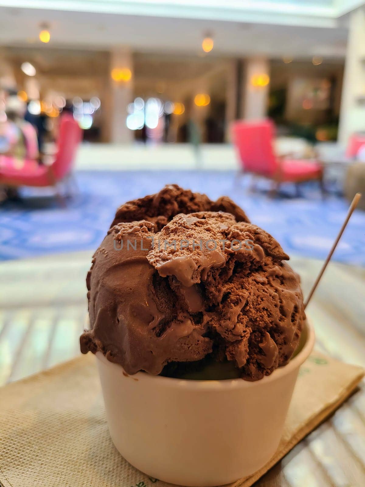 Close-up of rich and creamy chocolate ice cream in a white paper cup with wooden spoon, on a napkin, set in an elegant cafe in Nassau, Bahamas
