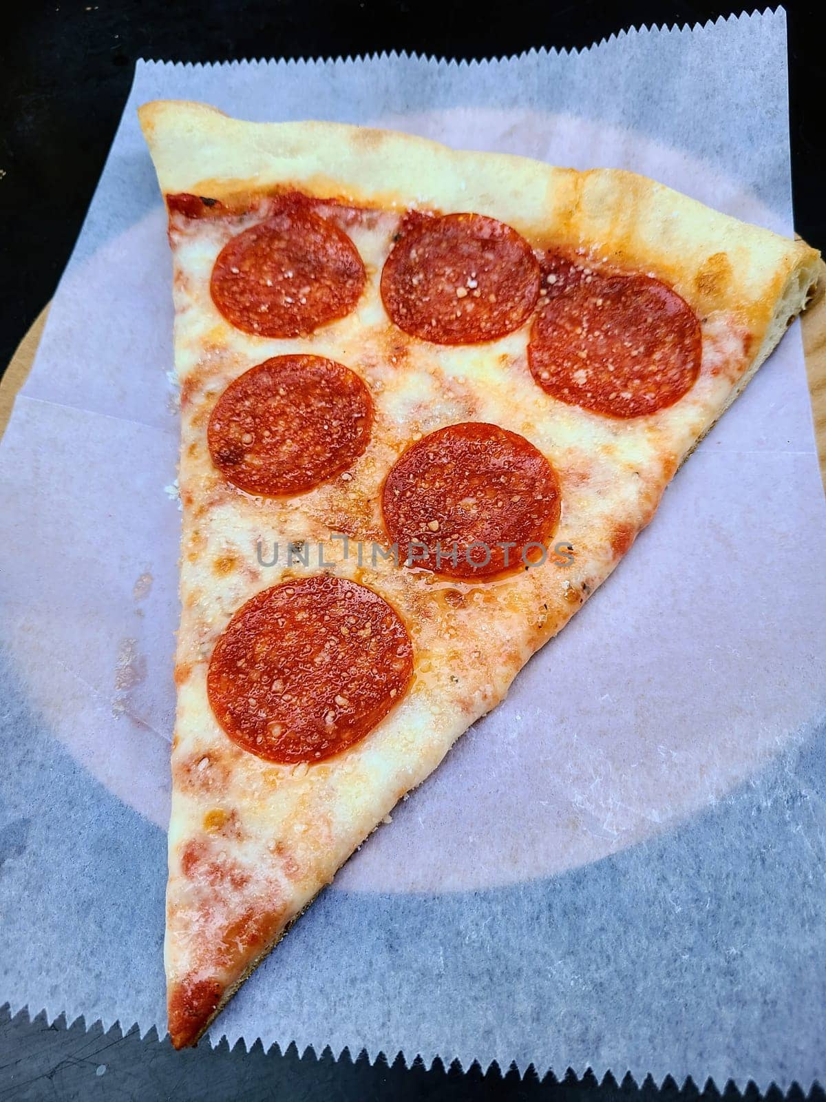 Freshly baked pepperoni pizza slice on parchment paper in New York City restaurant, 2022 - perfect for culinary and fast food concepts.