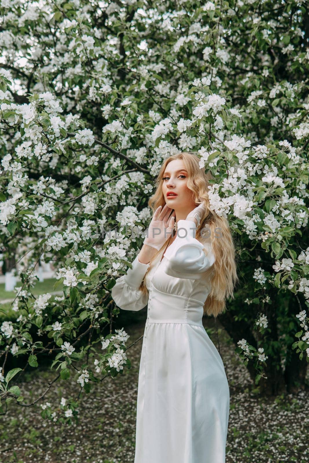 A blonde girl with long hair on a walk in a spring park. Springtime and blooming apple trees