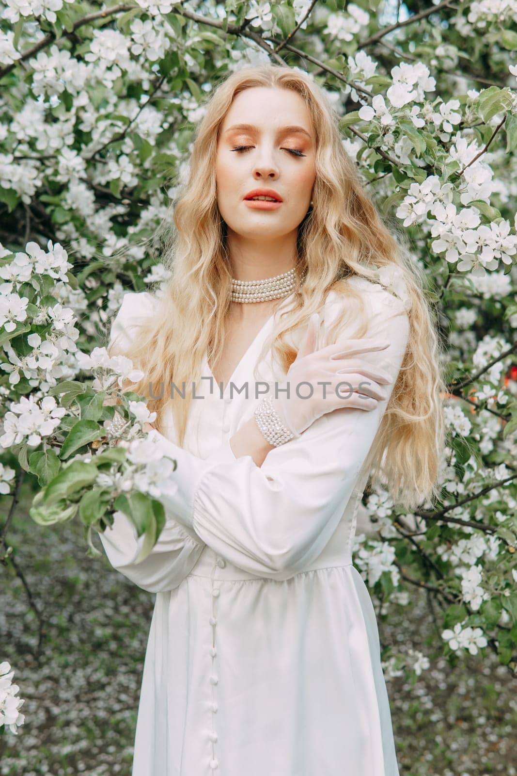 A blonde girl with long hair on a walk in a spring park. Springtime and blooming apple trees