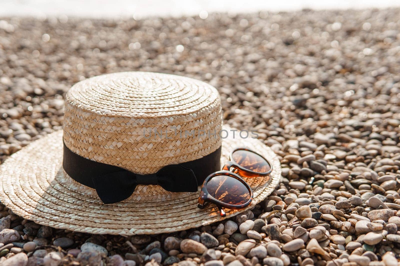 A straw hat and sunglasses on the beach. Pebbles on the seashore, close-up. The natural background.