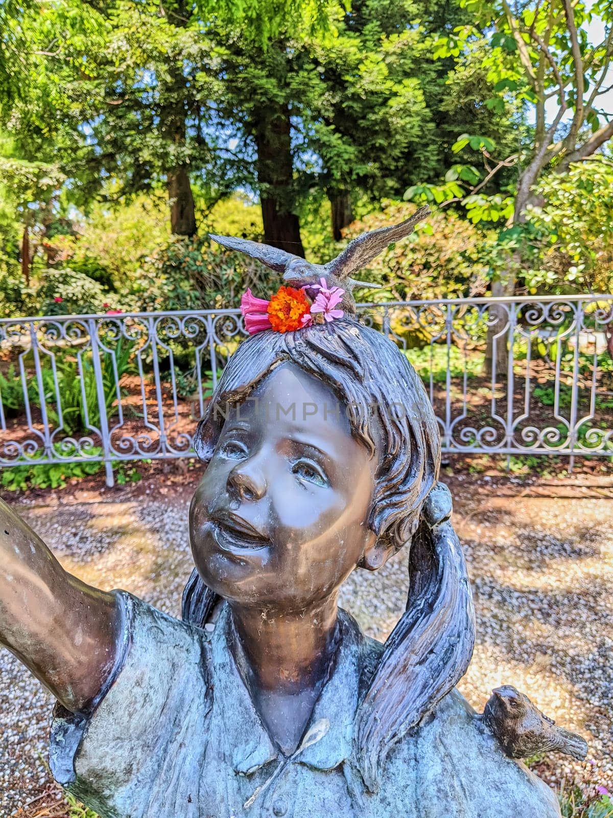 Joyful Bronze Statue of a Young Girl with Bird in a Lush Oakland Garden, California 2023
