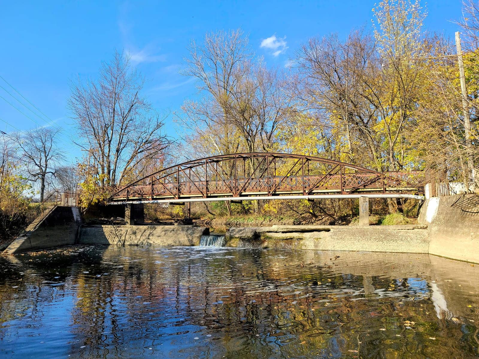 Tranquil autumn scene of a rustic metal bridge over a serene creek, framed by leafy trees in Fort Wayne, Indiana - 2022