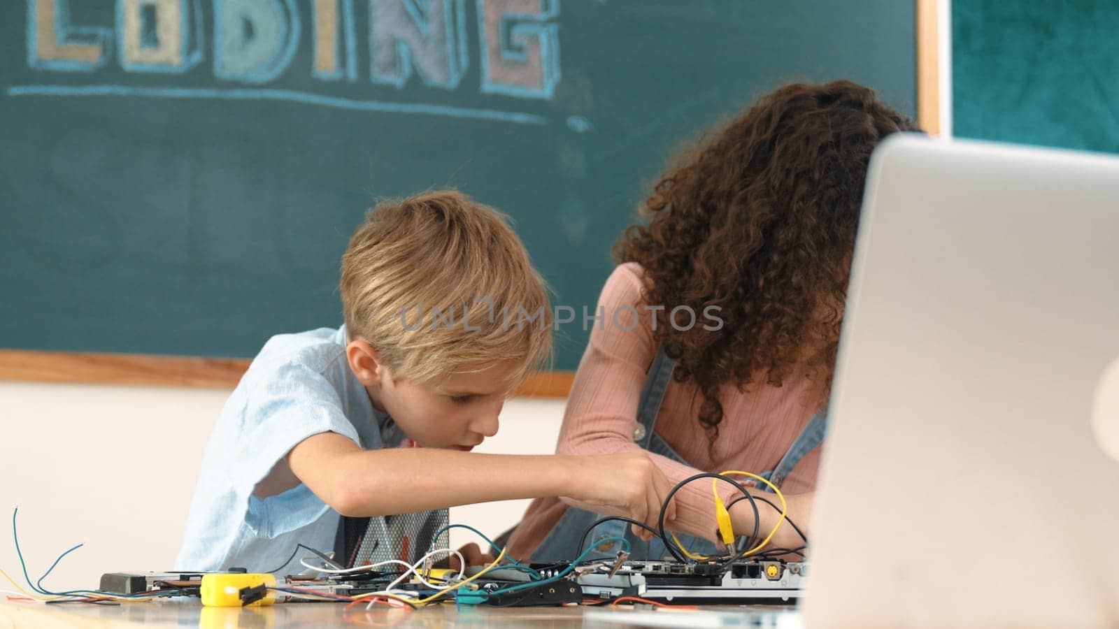 Diverse smart student working together to fix main board at stem class while looking at laptop screen at blackboard. Group of skilled children learning and studying about electronic machine. Pedagogy.