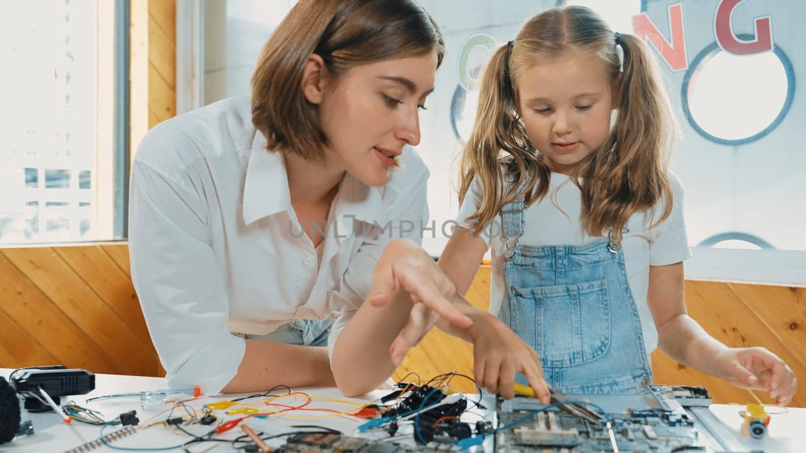 Young smart caucasian teacher teaching students about part of electronic board. Expert girl learn about digital electrical tool and fixing motherboard at table with chips and wires placed. Erudition.