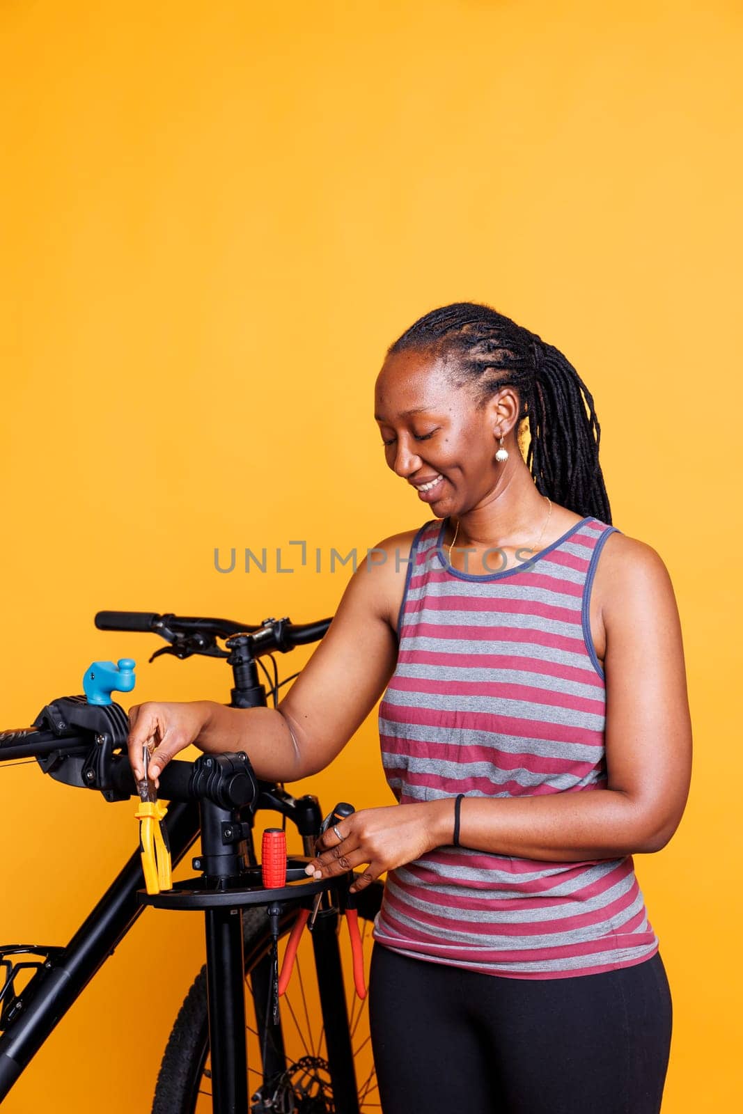 Energetic female cyclist grasping essential work tools to inspect and repair bicycle. Active african american woman holding and placing pliers, screwdrivers and other equipments for bike maintenance.