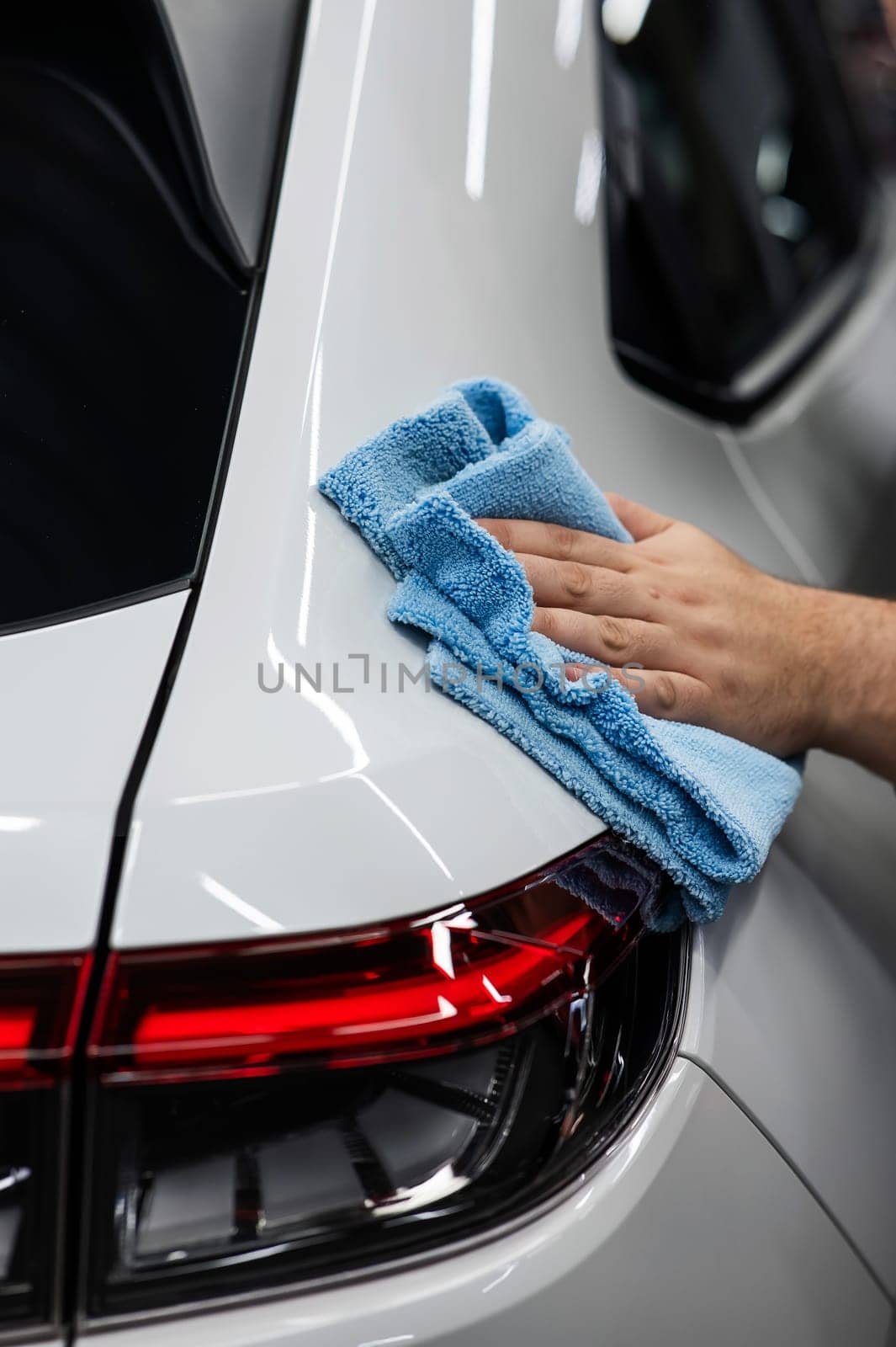 A mechanic wipes the body of a white car with a microfiber cloth. by mrwed54