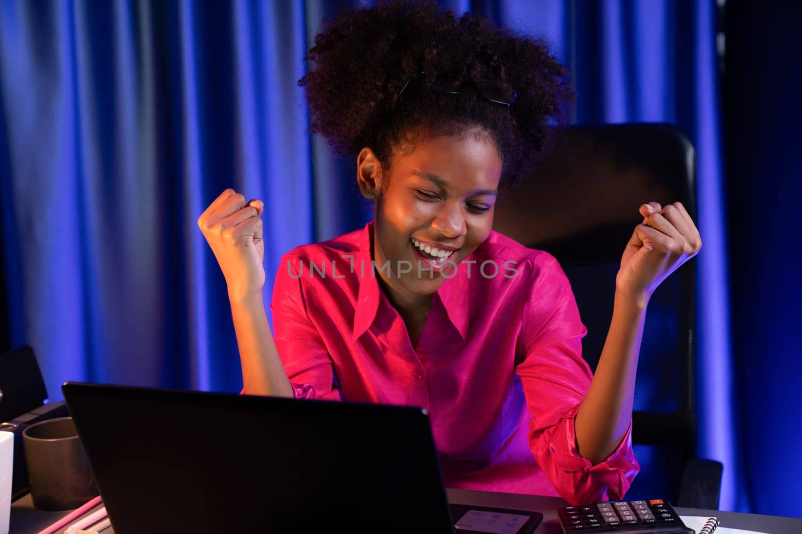 African woman blogger wearing pink shirt with happy face, looking on screen laptop with valued achievement project or get scholarship. Concept of cheerful expression work from home. Tastemaker.