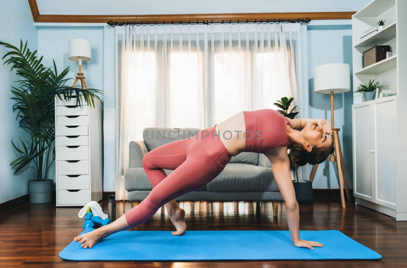 Flexible and dexterity woman in sportswear doing yoga position in meditation posture on exercising mat at home. Healthy gaiety home yoga lifestyle with peaceful mind and serenity.