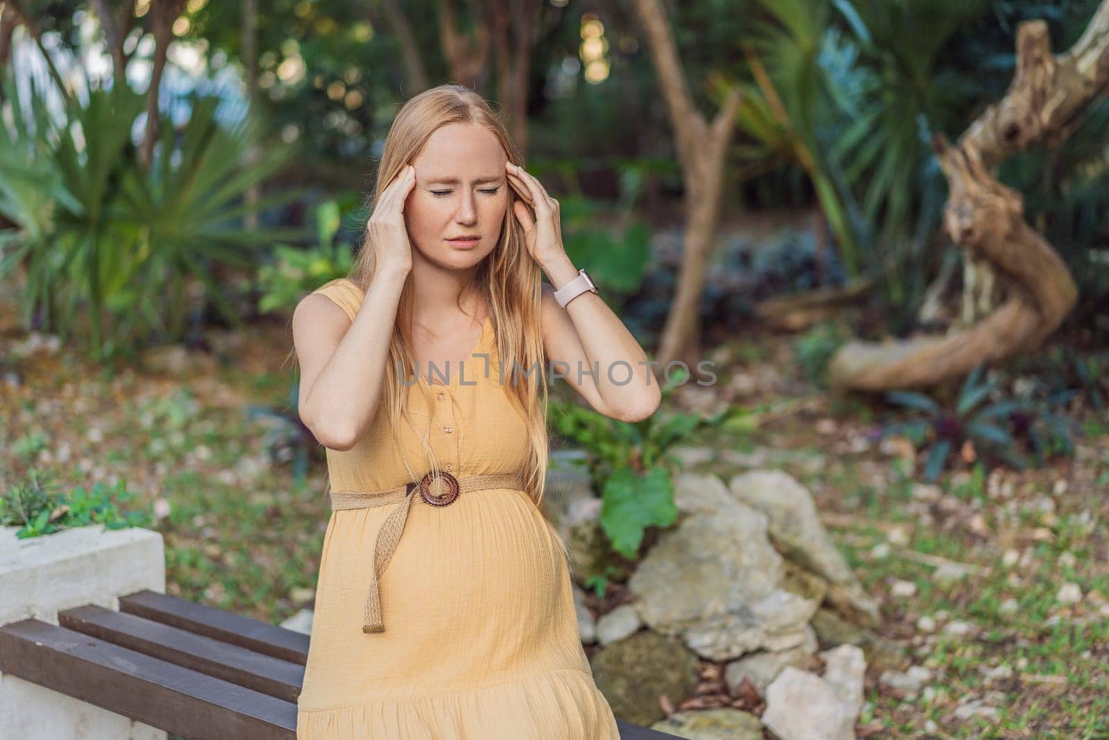 A pregnant woman experiences a moment of discomfort, grappling with a headache during pregnancy, highlighting the common challenge and the need for proper self-care and attention to maternal well-being.