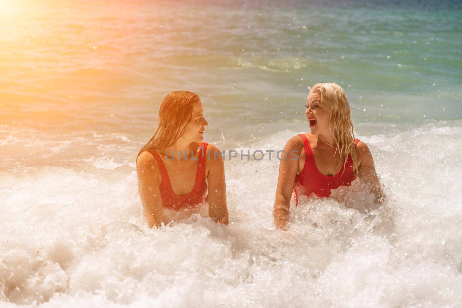 Women ocean play. Seaside, beach daytime, enjoying beach fun. Two women in red swimsuits enjoying themselves in the ocean waves. by Matiunina