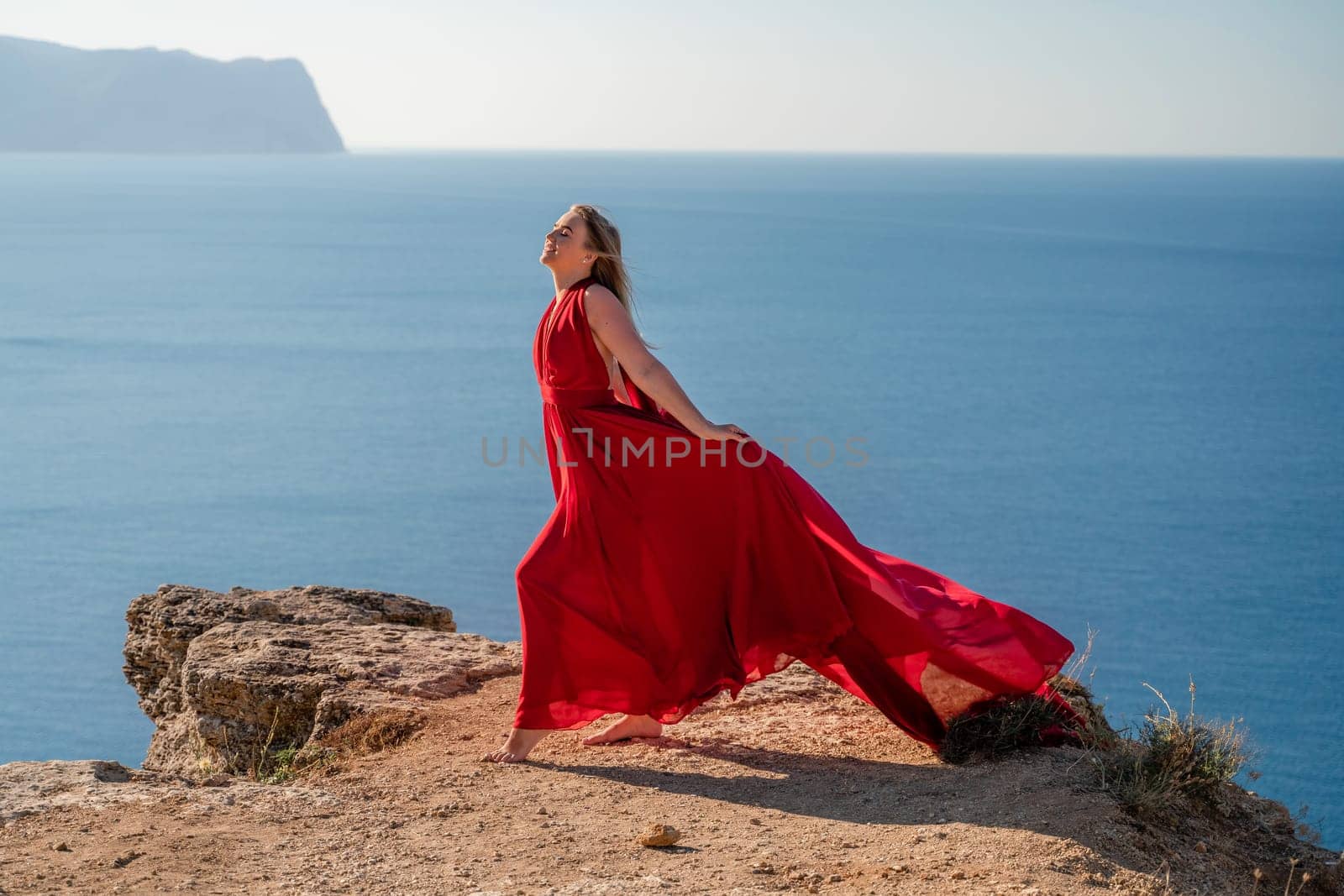 A woman in a red flying dress fluttering in the wind, against the backdrop of the sea