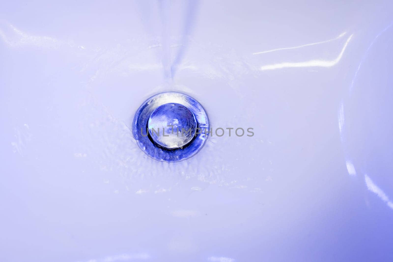 stream of clean water flows into in blue tones. Sink plug hole close up macro.