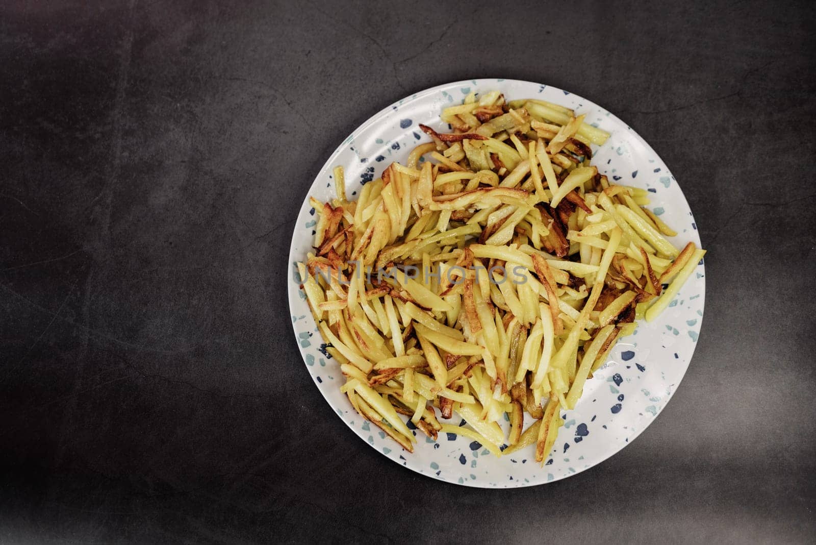golden fried potatoes in a plate on a dark background with a copy space