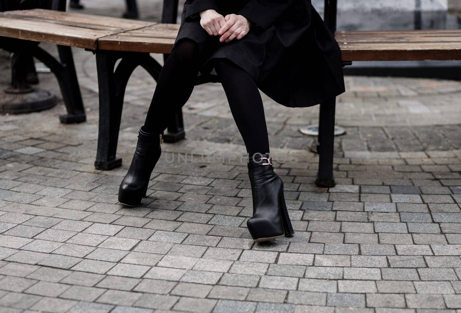 woman in black coat and leather boots with heel sitting on bench