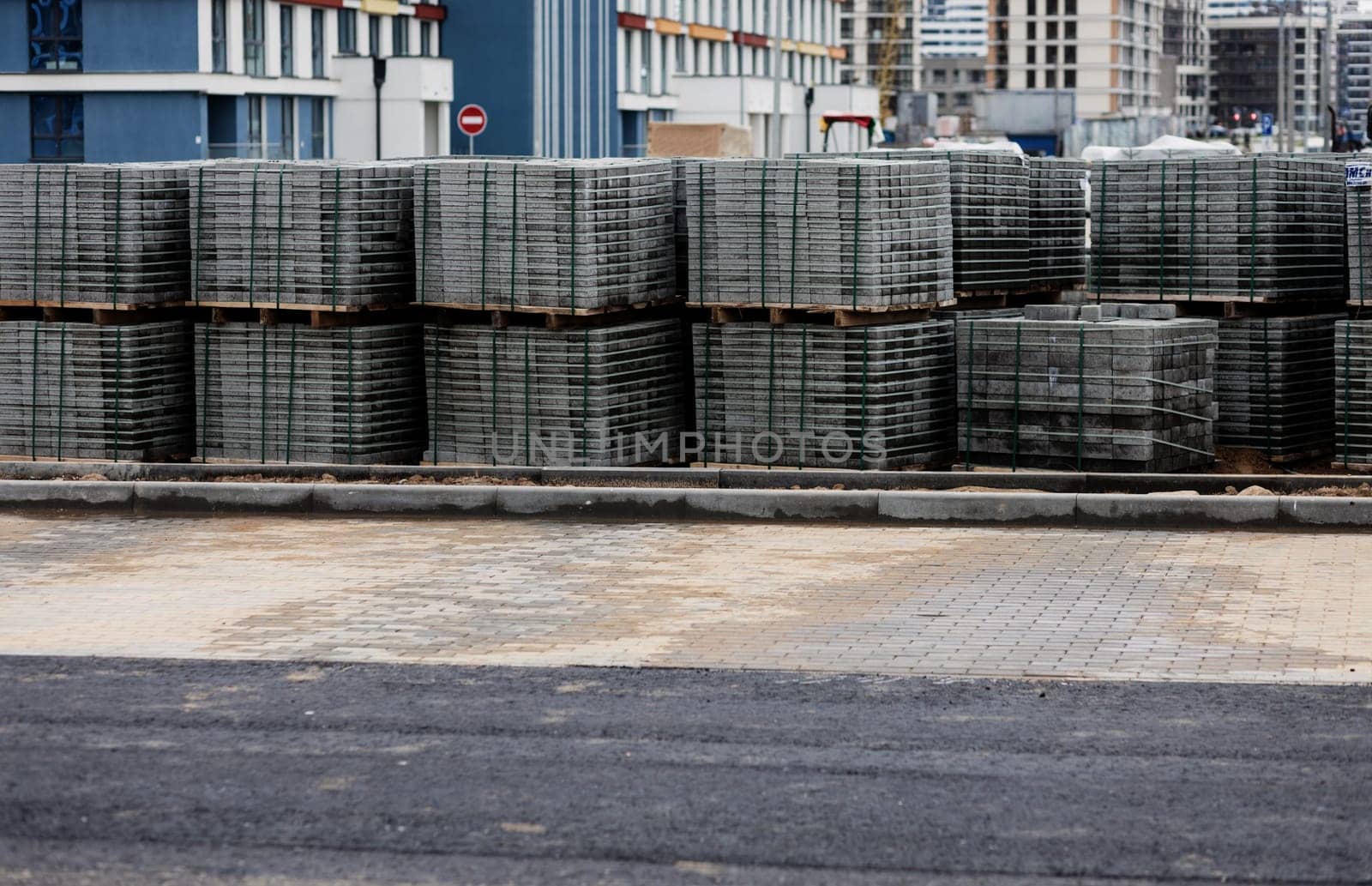 tiles, made of concrete, are designed to repair the sidewalk and are stacked on wooden pallets that stand near the sidewalk