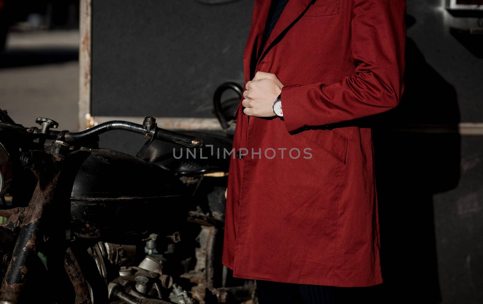 Young handsome man in a red coat near a vintage motorcycle
