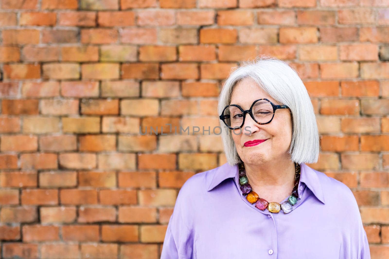 portrait of beautiful senior woman in glasses winking looking at camera, concept of happiness of elderly people and active lifestyle, copy space for text