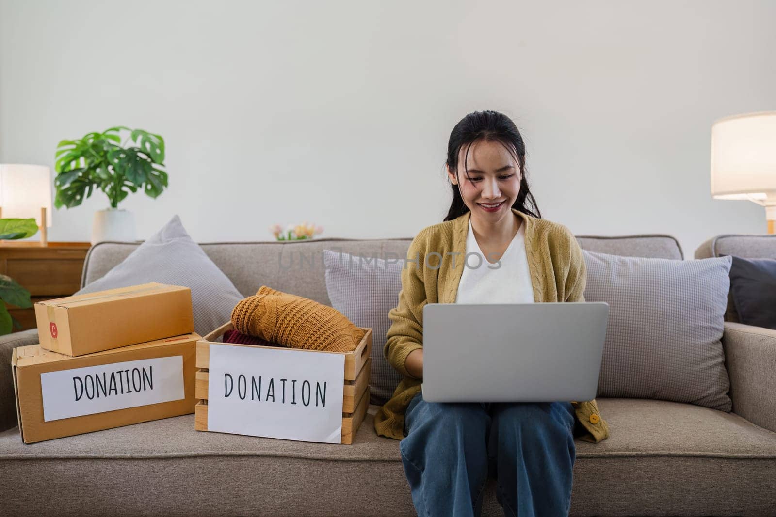 Asian young woman using laptop for donate box with second hand clothes. Donate concept by itchaznong