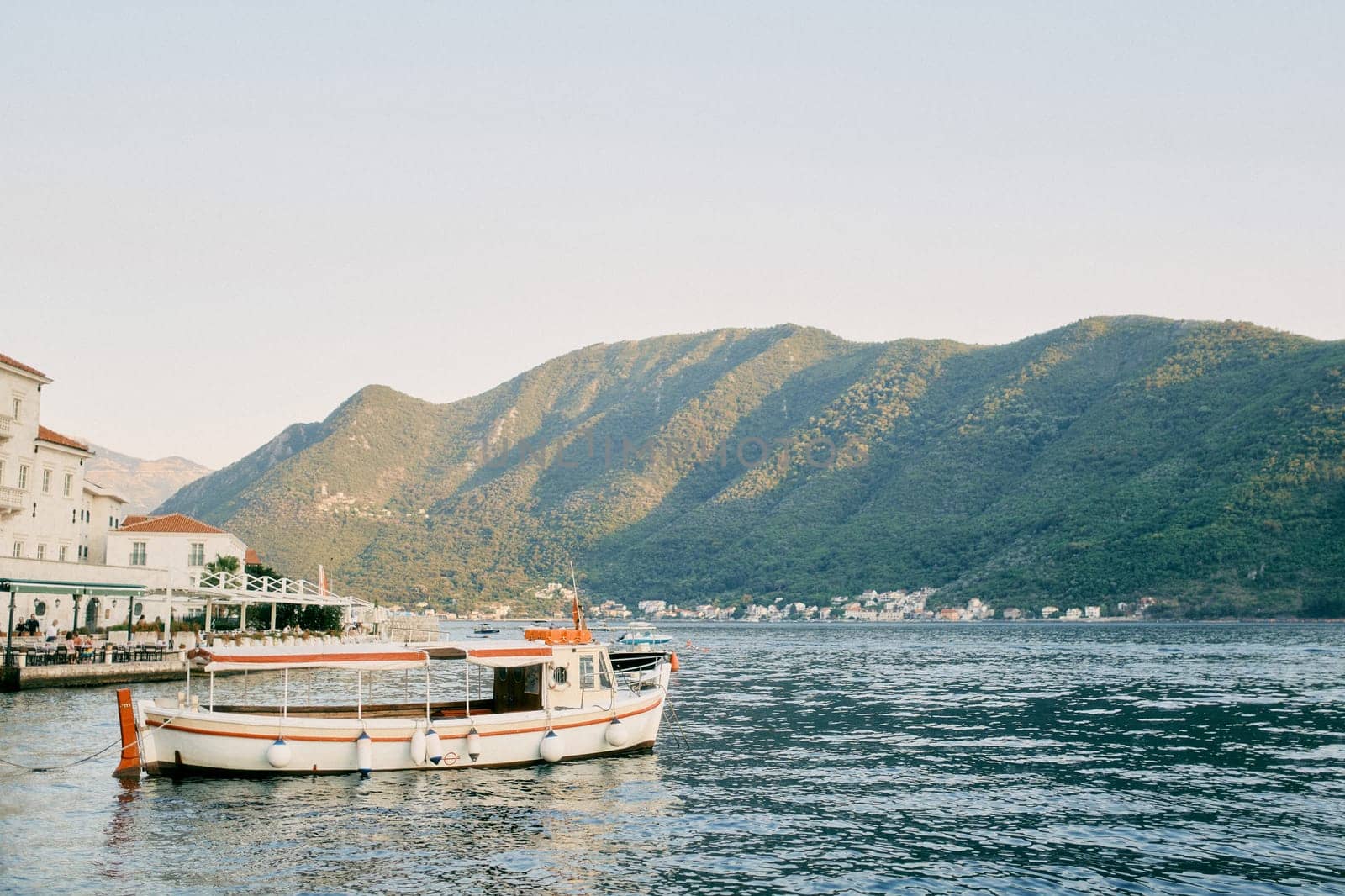 Tour boat is moored near the promenade with covered open-air restaurants. Perast, Montenegro. High quality photo