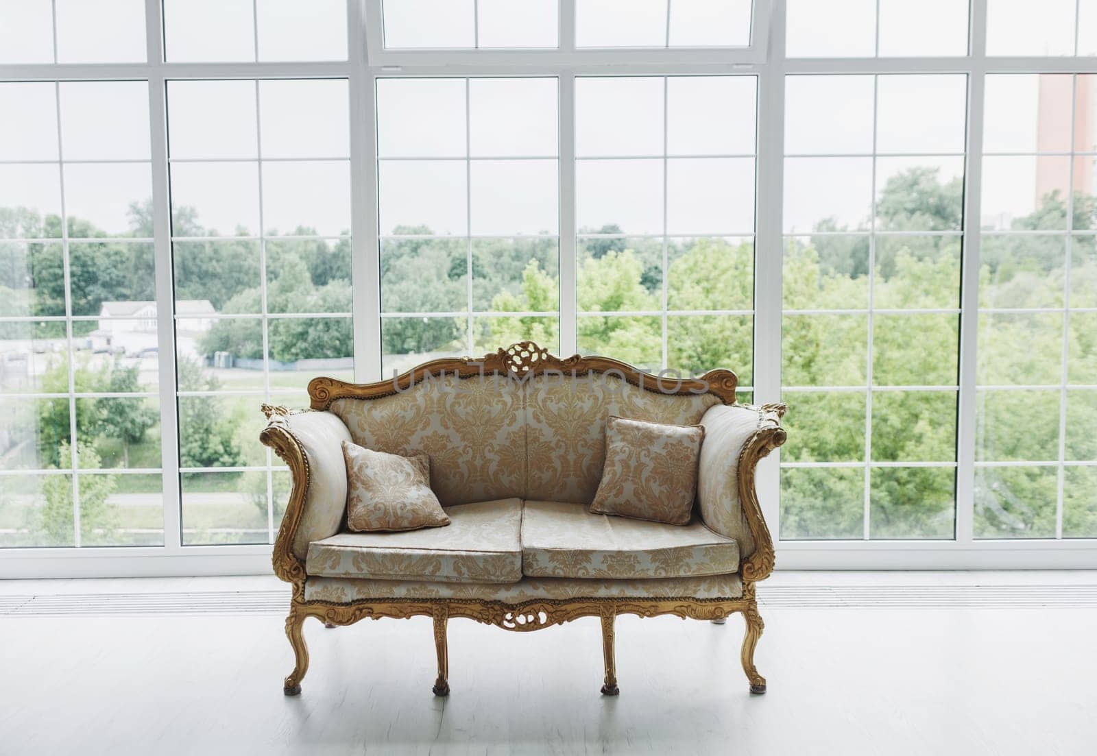 Vintage royal sofa with carved inserts upholstered in fabric on the background of a large window