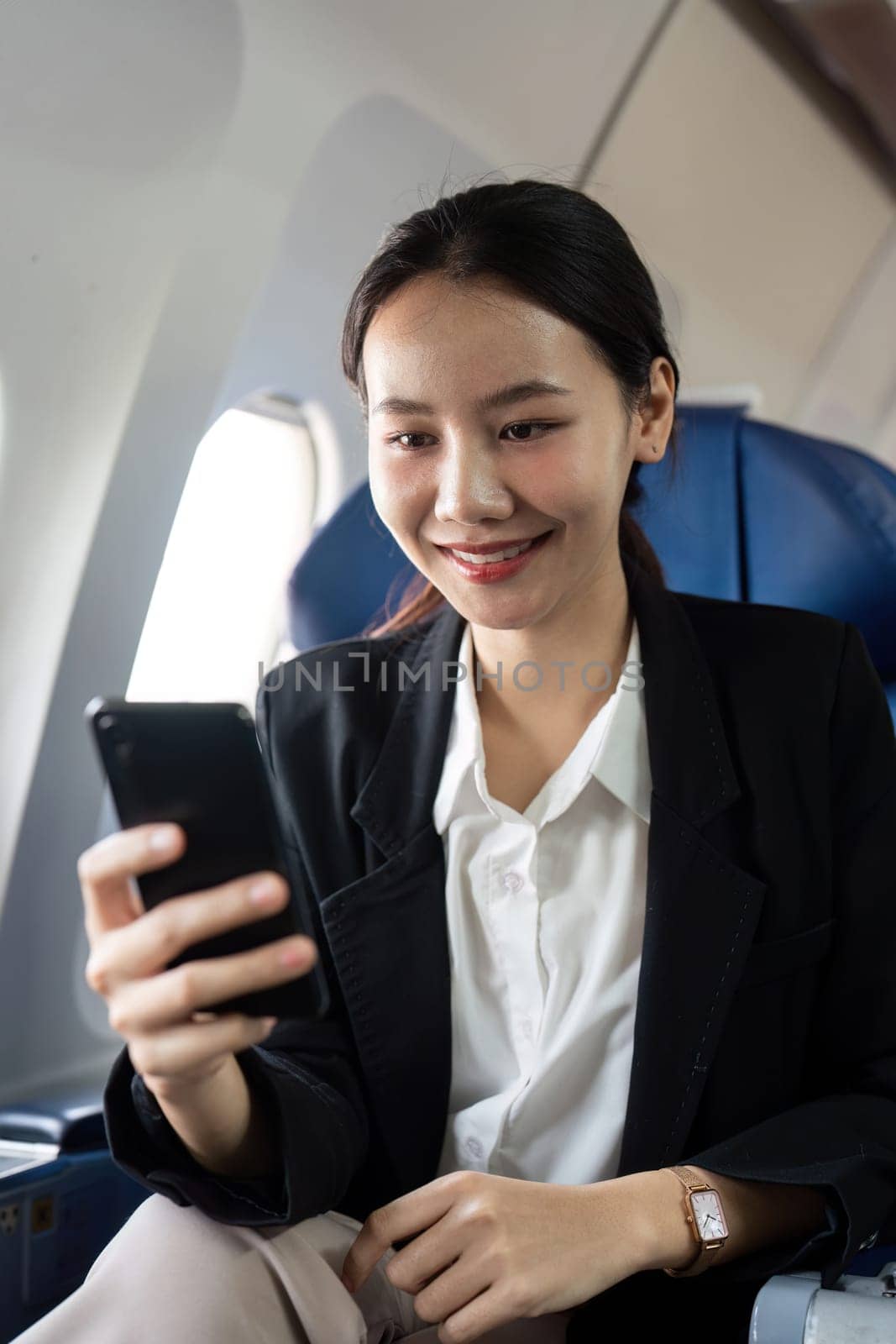 Asian young businesswoman successful or female entrepreneur in formal suit in a plane sit in a business class seat and uses a smartphone during flight. Traveling and Business concept by nateemee