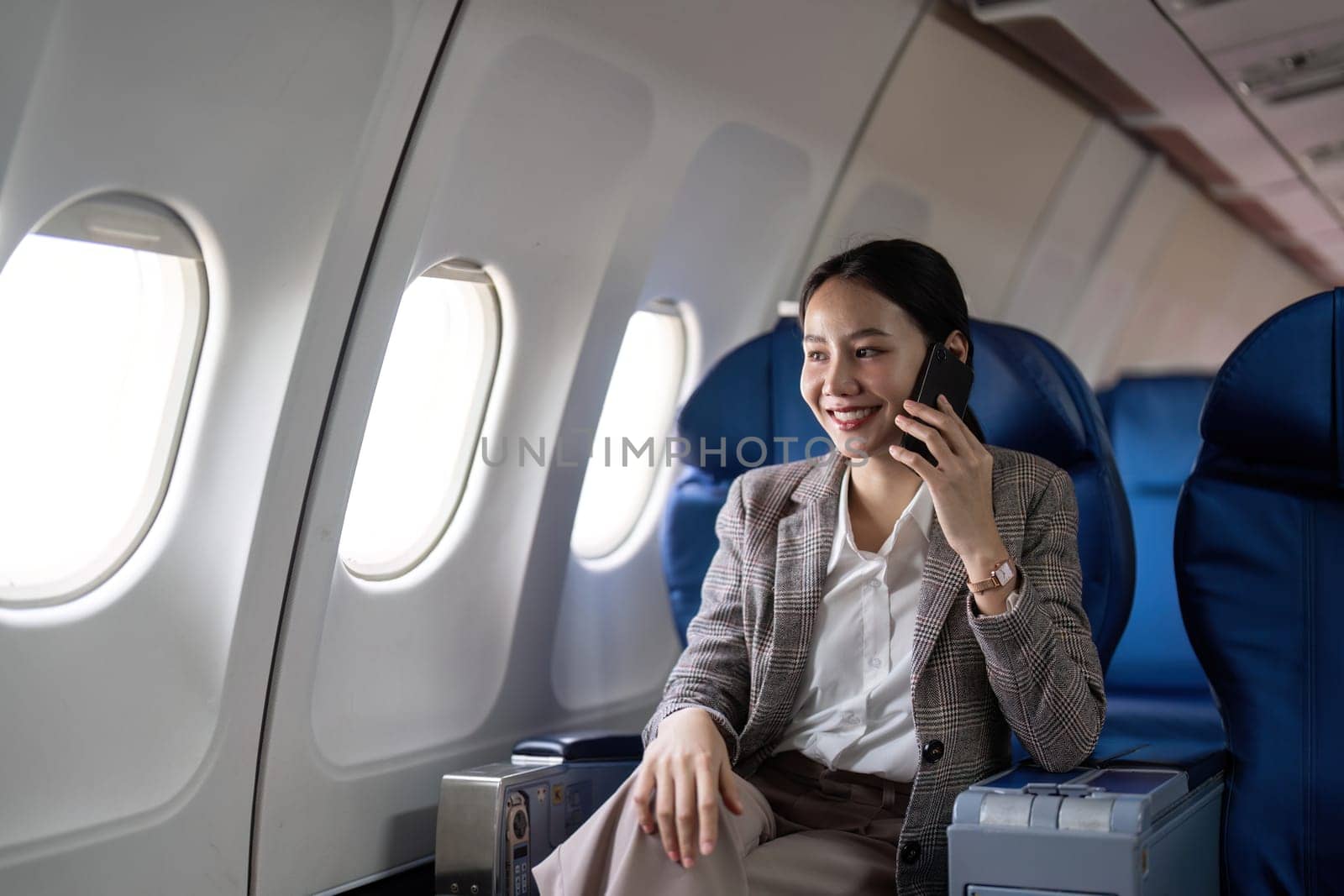 Asian young businesswoman successful or female entrepreneur in formal suit in a plane sit in a business class seat and uses a smartphone during flight. Traveling and Business concept.