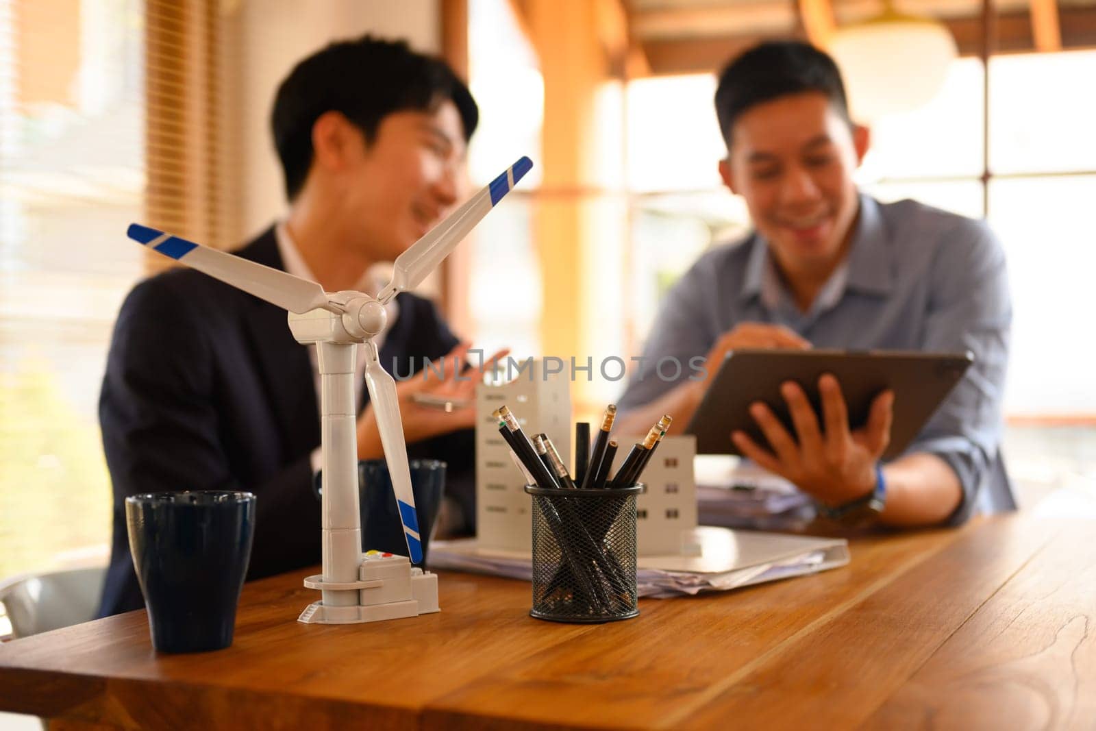 A wind turbine model on table with two businessman working in background. Alternative energy concept.