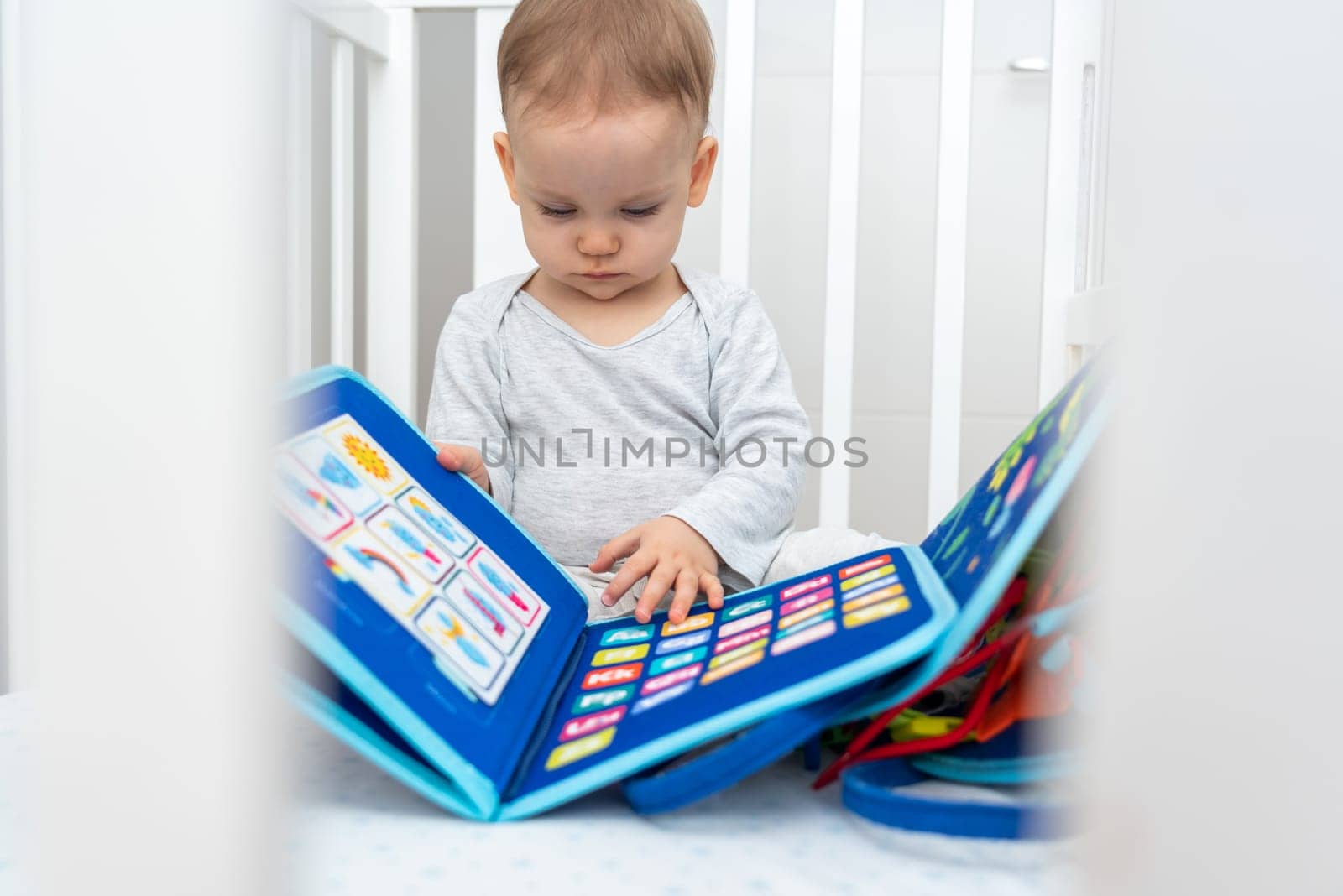 Baby playing with montessori quiet book sitting in a crib. Concept of smart books and modern educational toys by Mariakray