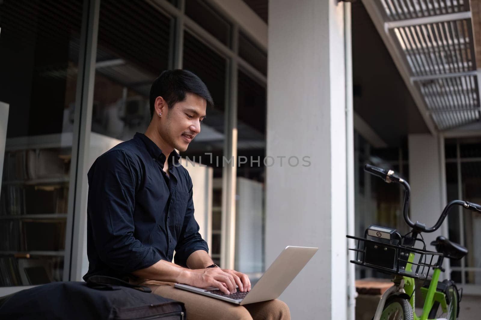 A young Asian businessman rides a bicycle to work. Use a reusable water bottle. Working outside of the office using a laptop The concept of saving energy and reducing pollution to the environment..