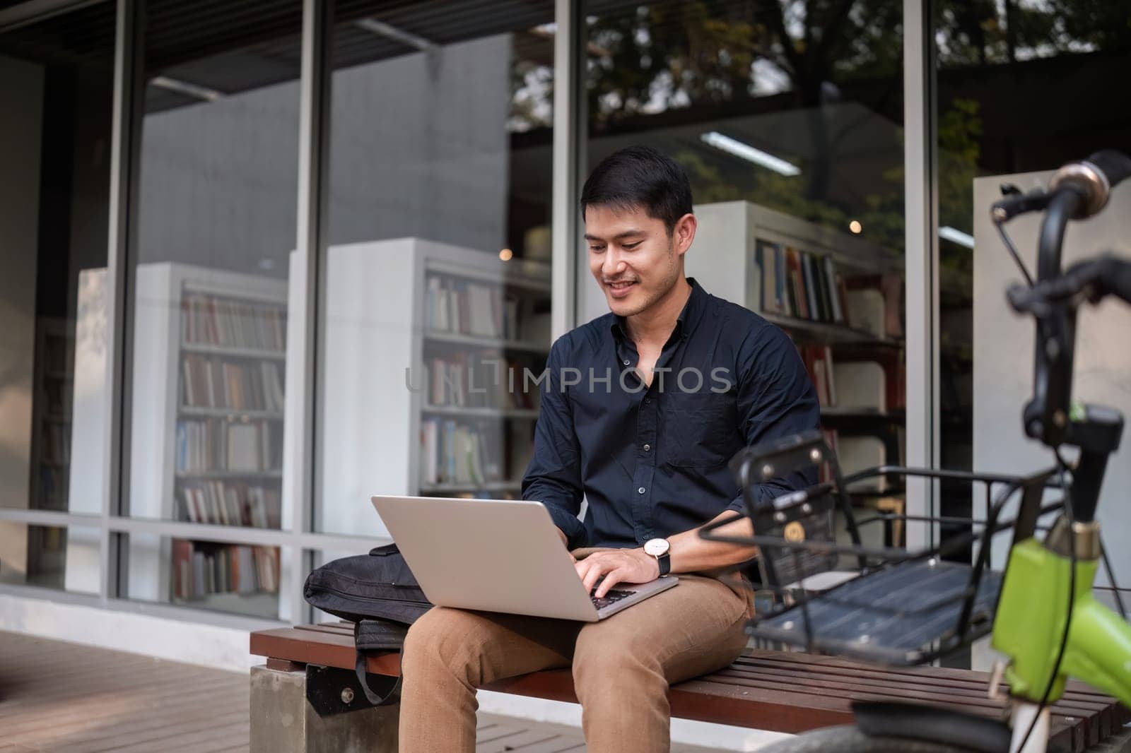 A young Asian businessman rides a bicycle to work. Use a reusable water bottle. Working outside of the office using a laptop The concept of saving energy and reducing pollution to the environment..