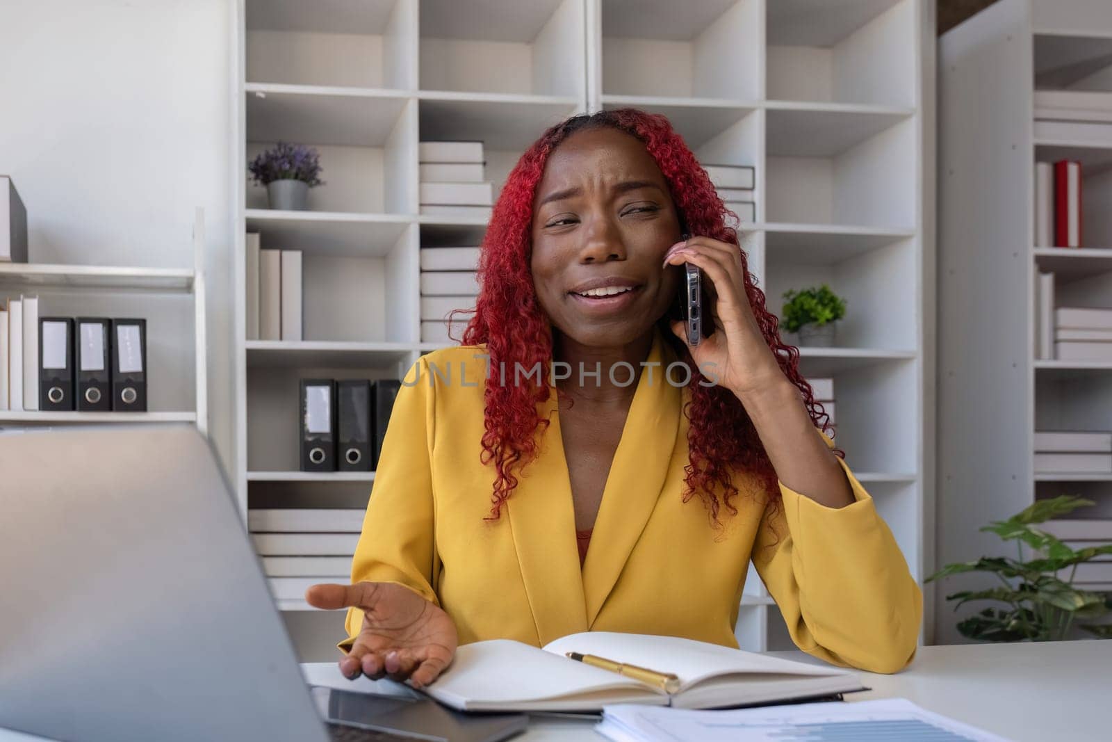 Young African American business woman talking on the phone and taking notes while working in the office.