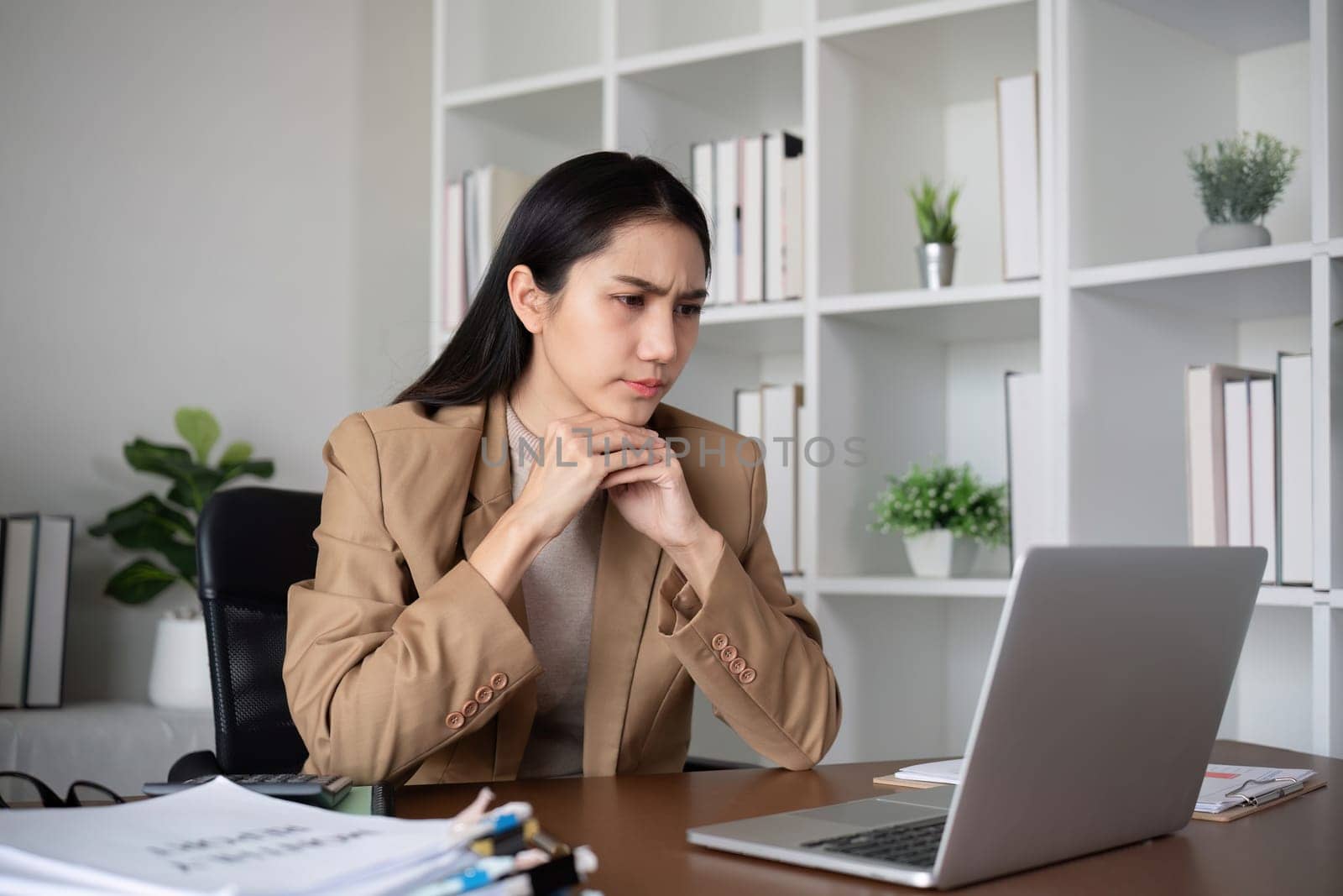 Unhappy Asian business woman shows stress over unsuccessful business while working in home office decorated with soothing green plants. by wichayada