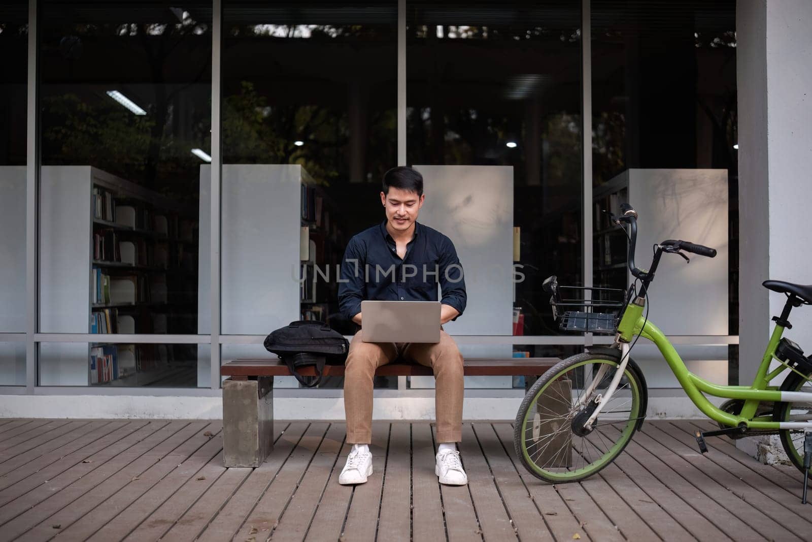 A young Asian businessman rides a bicycle to work. Use a reusable water bottle. Working outside of the office using a laptop The concept of saving energy and reducing pollution to the environment..