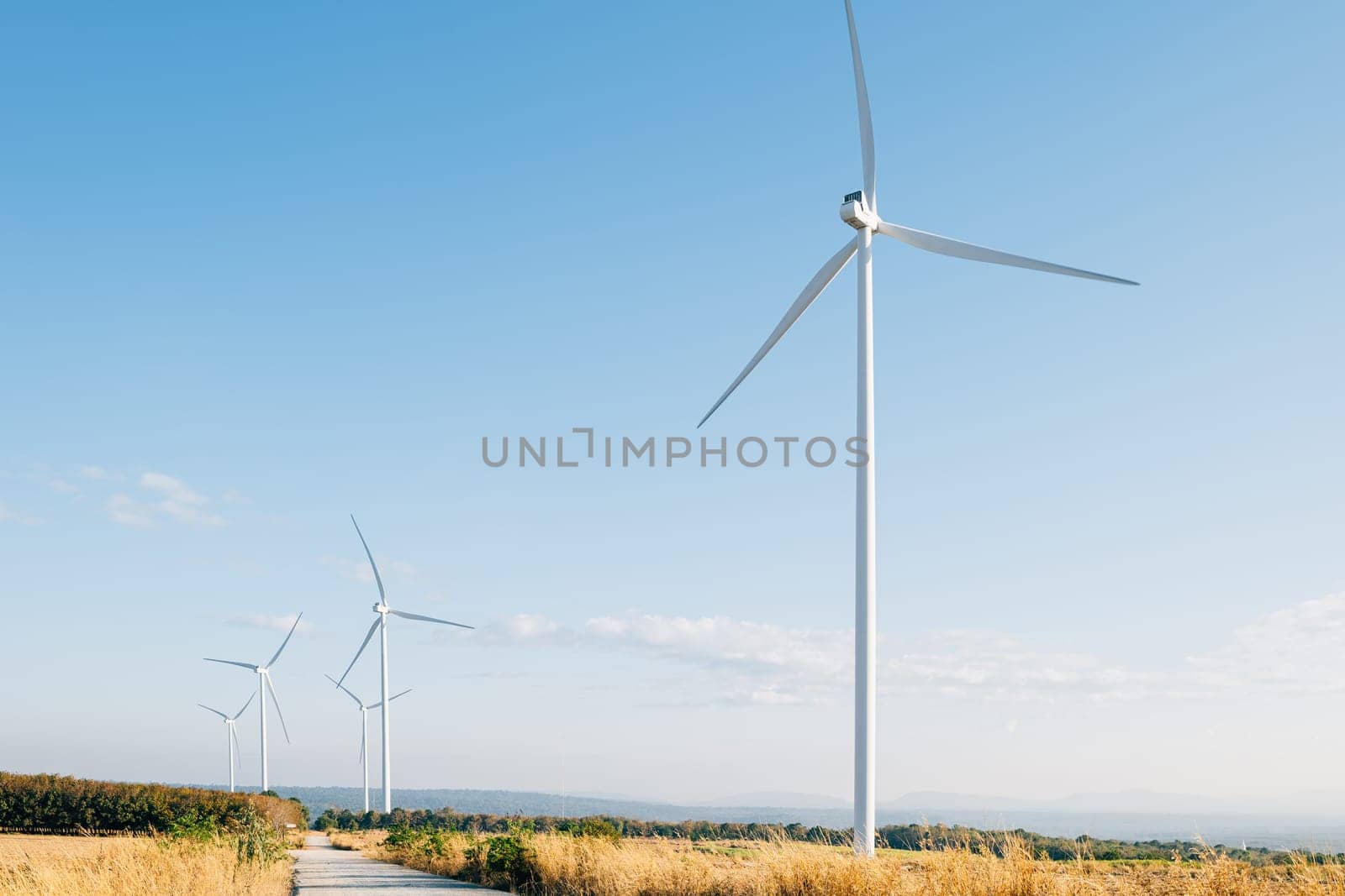 A mountain windmill farm signifies sustainable innovation with turbines harnessing clean wind energy. Modern technology shaping a green future against a vivid blue sky.