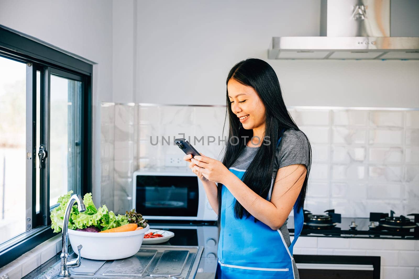 In a cozy kitchen an Asian woman cooks vegetables while browsing her smartphone for a cooking tutorial. Smiling and inspecting fruits she integrates modern tech into her cooking process.