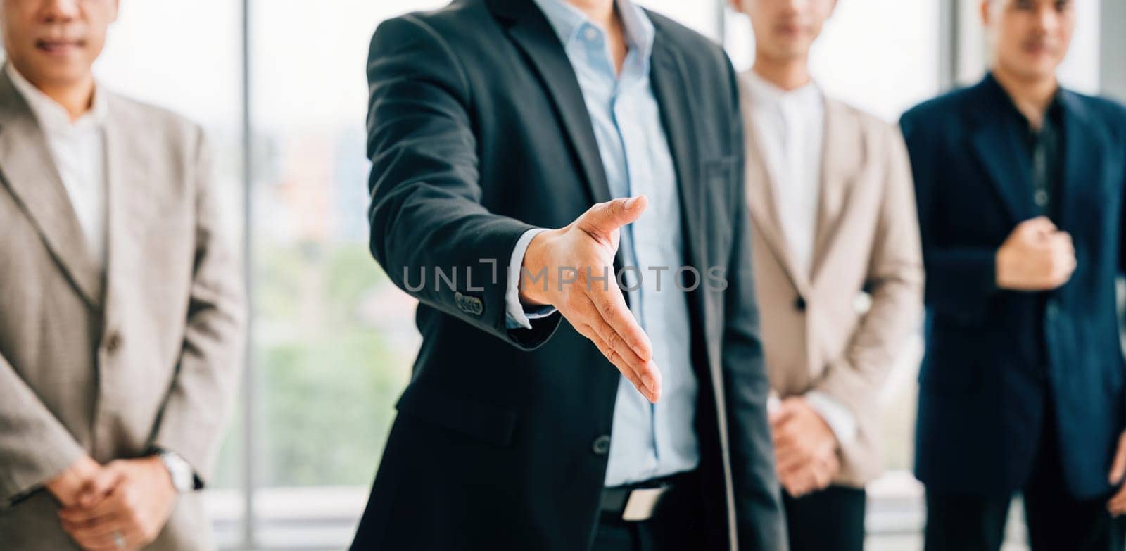 Businessman in suit extends his open palm in gesture of request and handshake, symbolizing trust successful cooperation and teamwork in office setting. It represents professionalism and confidence. by Sorapop