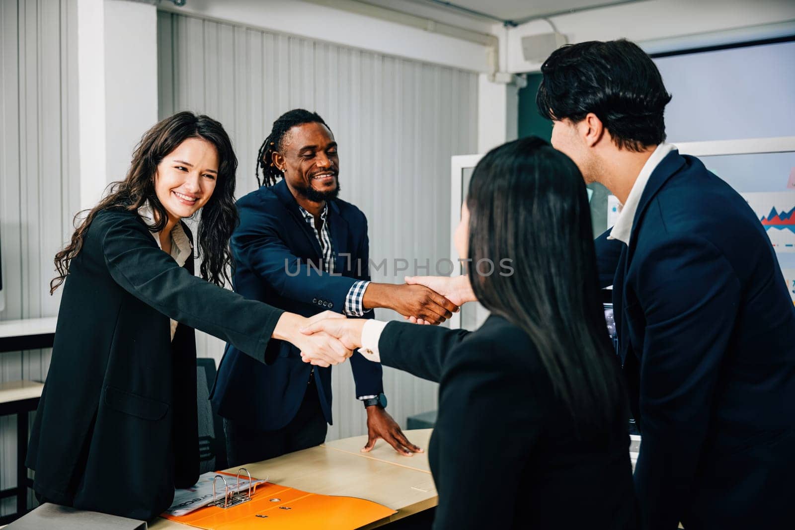 In an office, business people shake hands to celebrate an agreement. Colleagues, including marketing experts, successfully conclude a deal after a productive meeting. Teamwork by Sorapop