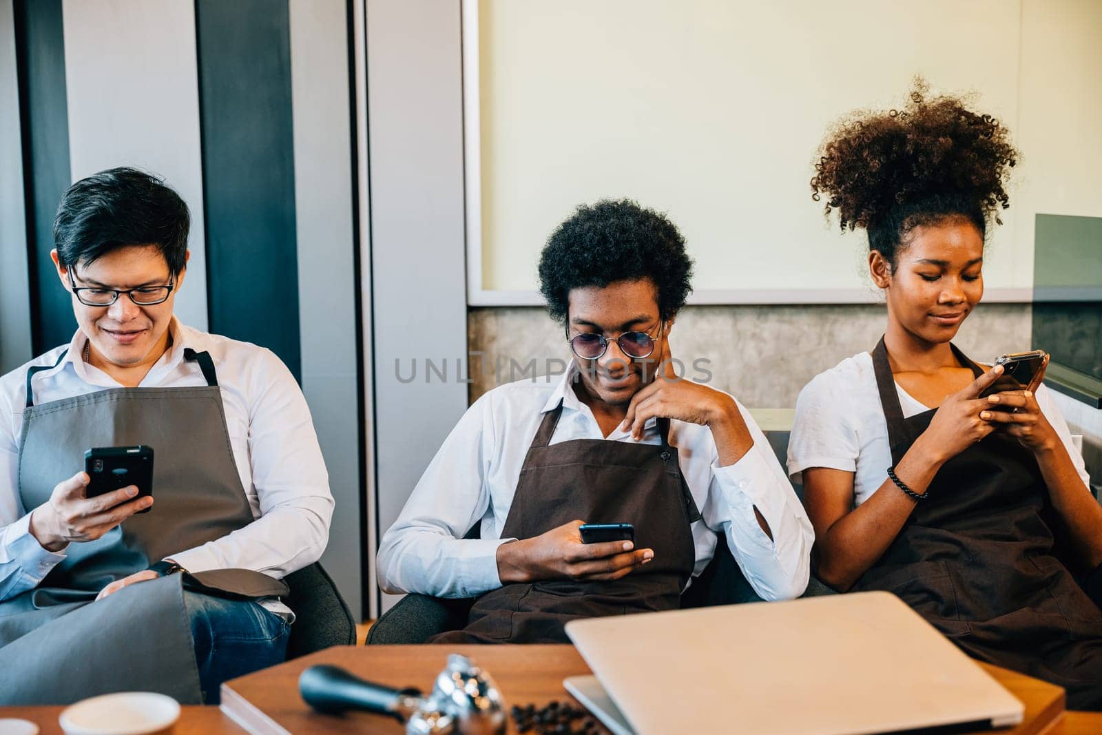 A diverse group of baristas gathered in a cafe using phones enjoying relaxation. Professionals in uniform embrace teamwork and connection through smartphone interaction. No order